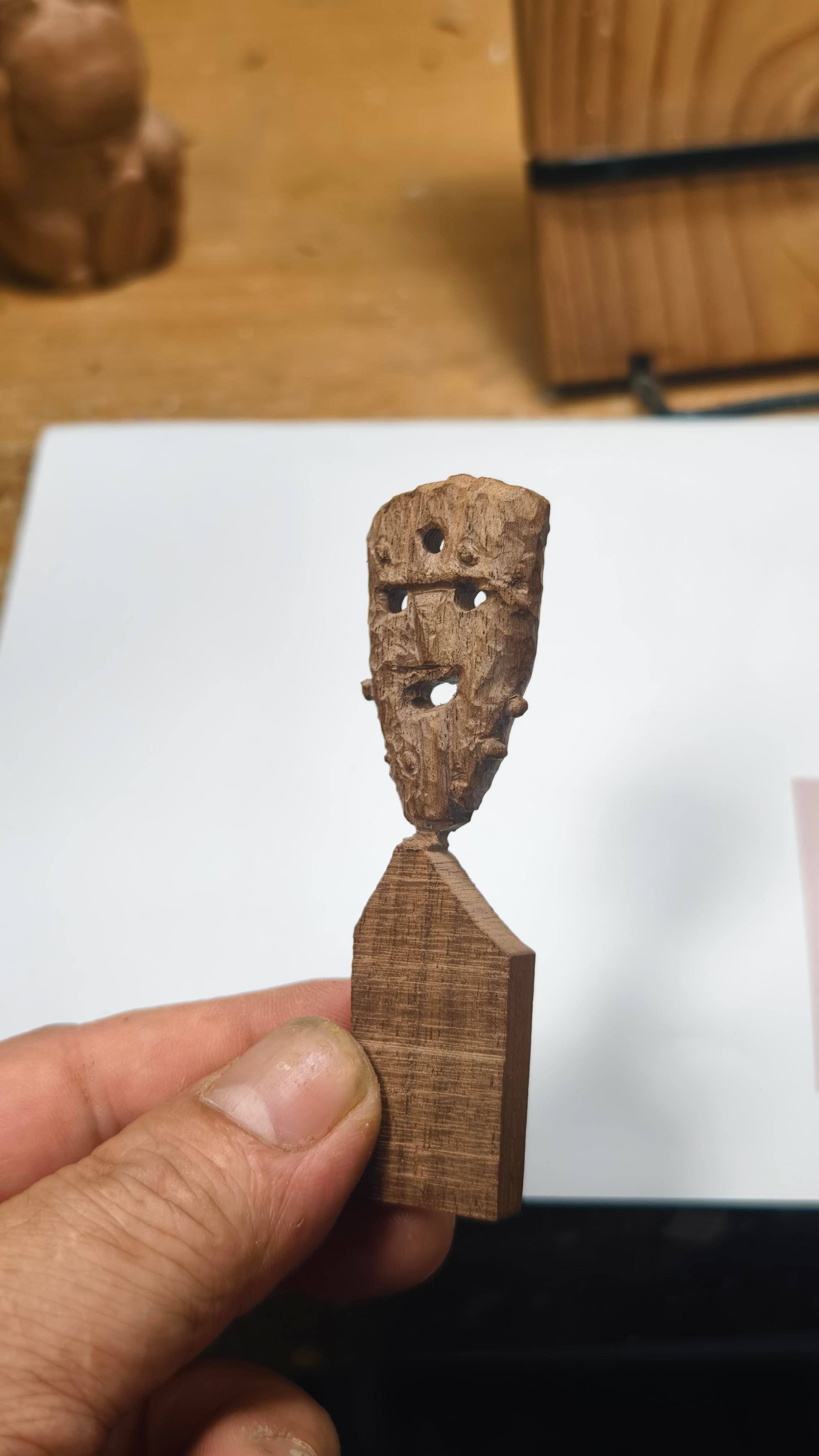 Small wooden sculpture of a figure held by a hand on a white surface.
