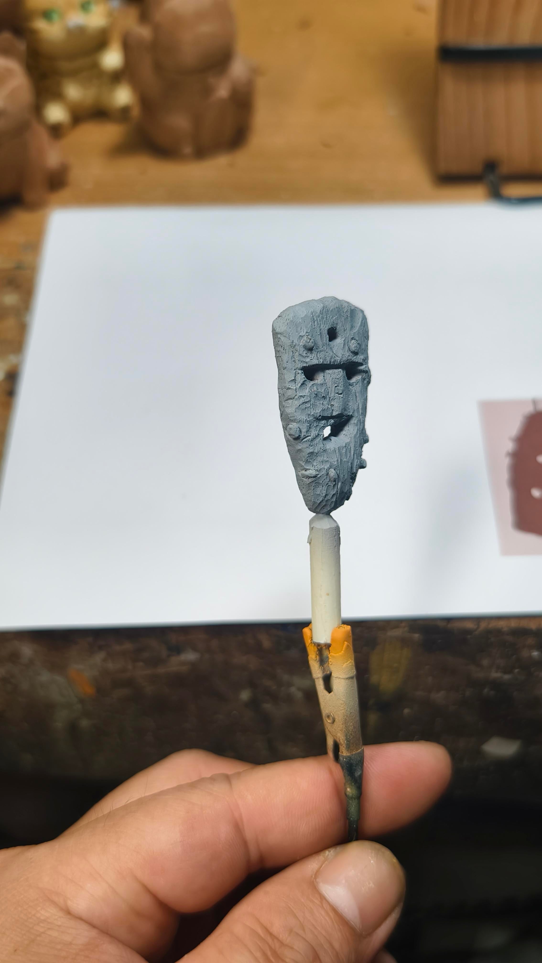 Small Icelandic mask gríma a face held by a hand on a wooden surface with a white paper in the background.
