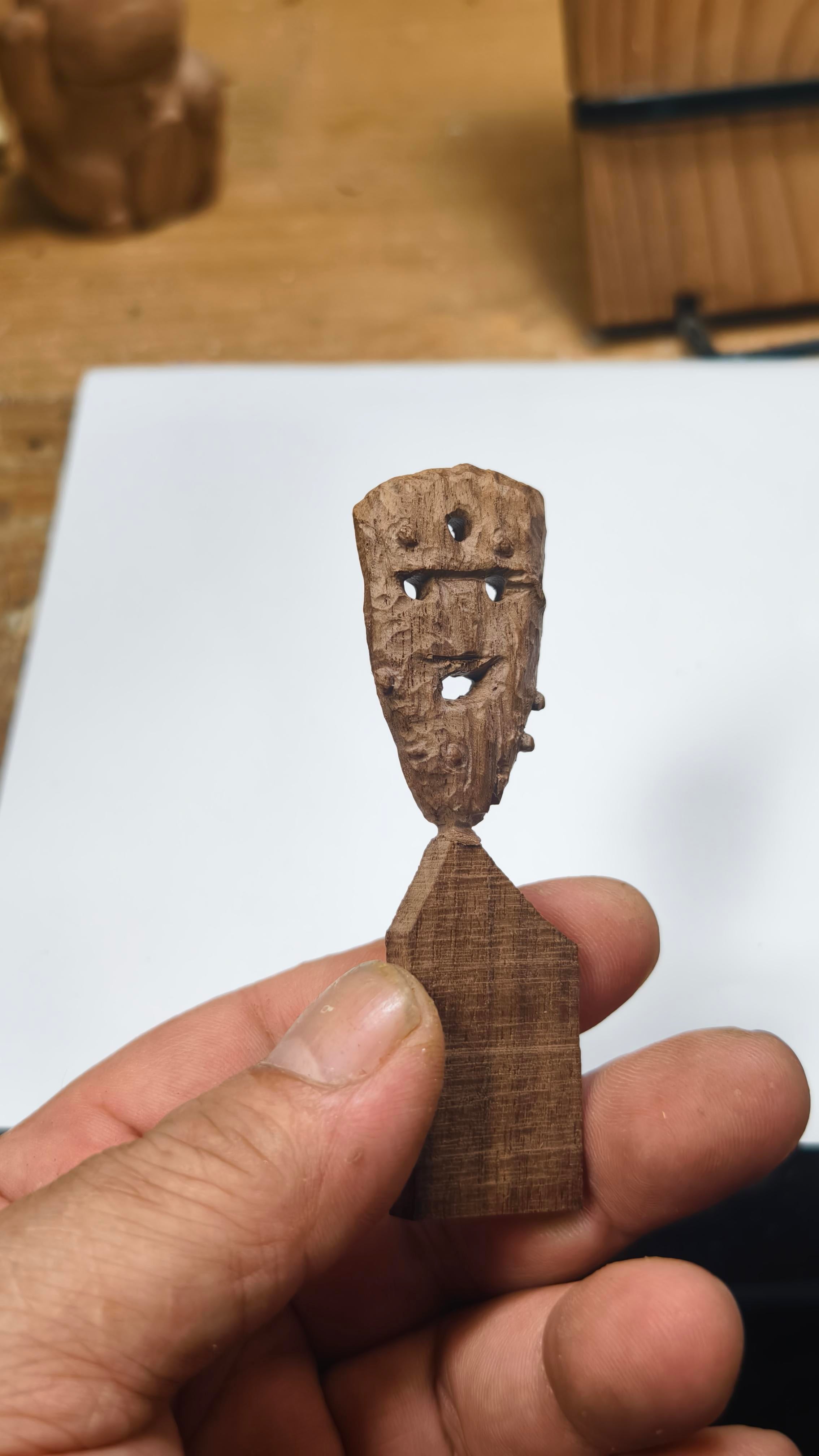 Small wooden figurine held in a hand on a blurred background