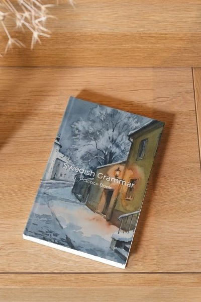 Book on a wooden surface next to a vase with dried plants and a gray cushion.