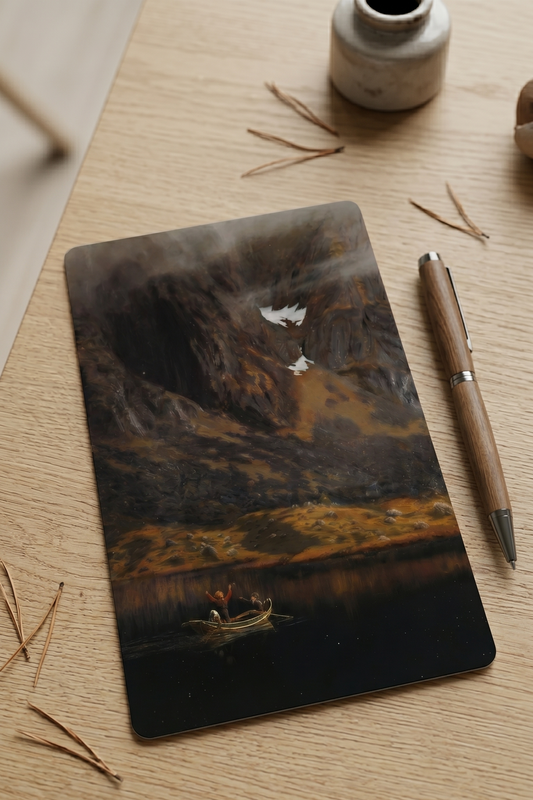 Notebook with a mountain landscape design on a wooden surface with a pen and small vase.