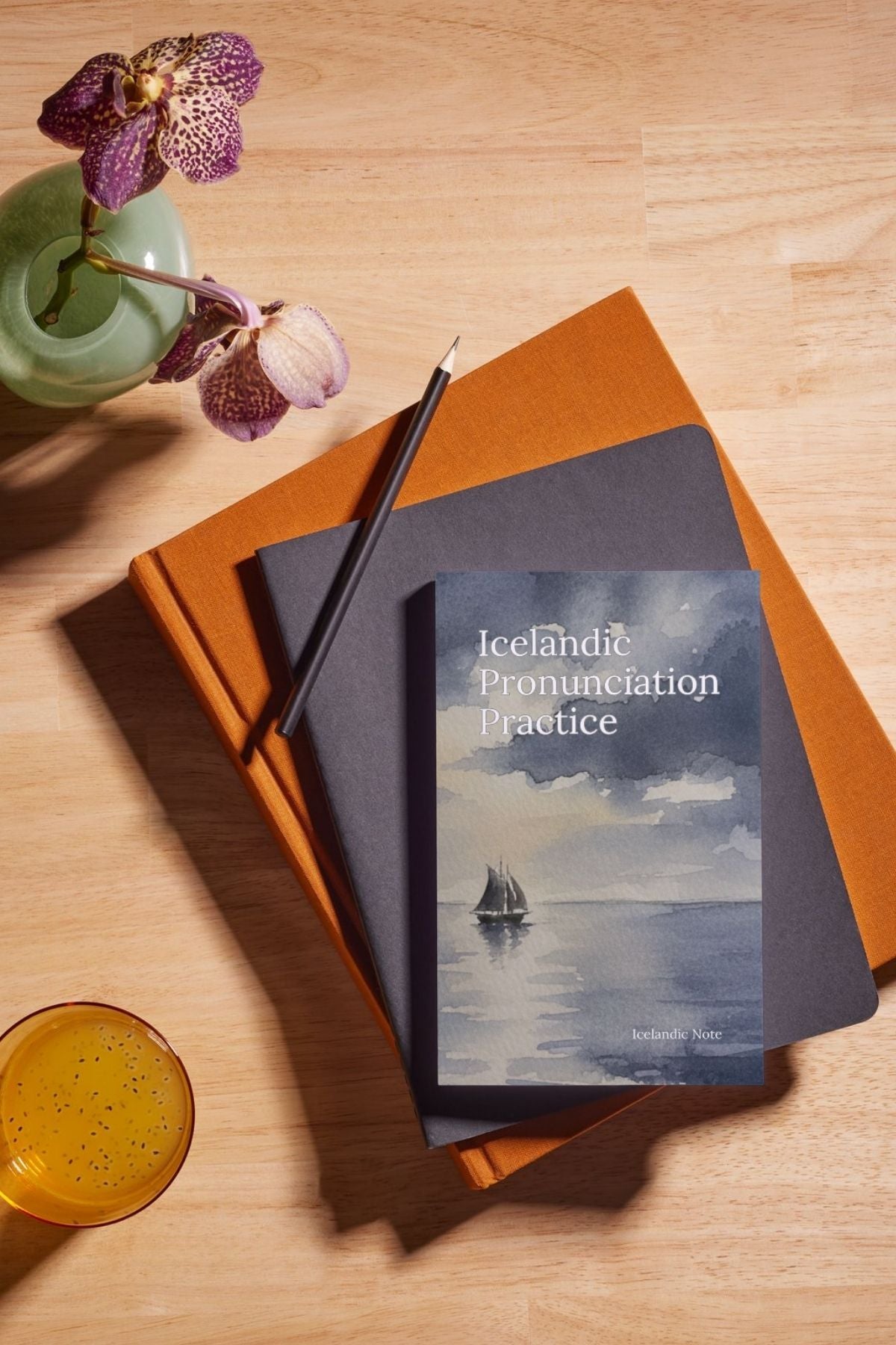Book titled 'Icelandic Pronunciation Practice' on a wooden surface with a pencil and flower.